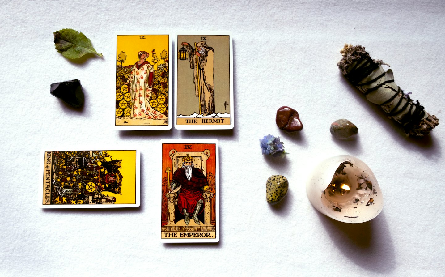 Tarot cards, crystals, sage, and a lit candle for spiritual practice.