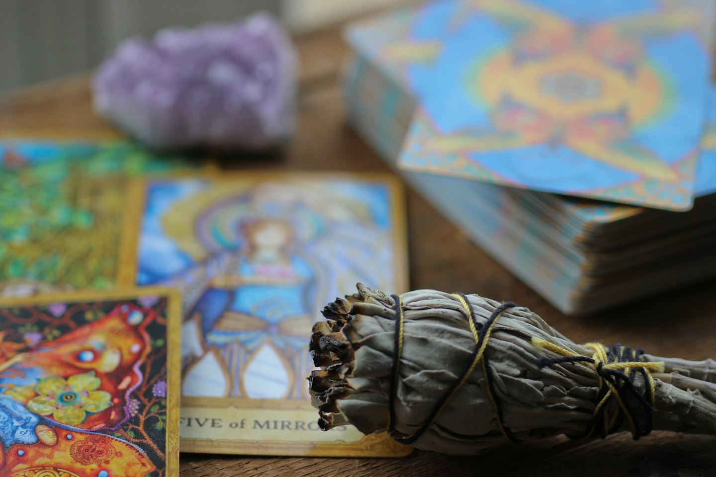Sage, tarot cards, and amethyst crystal on wooden surface.